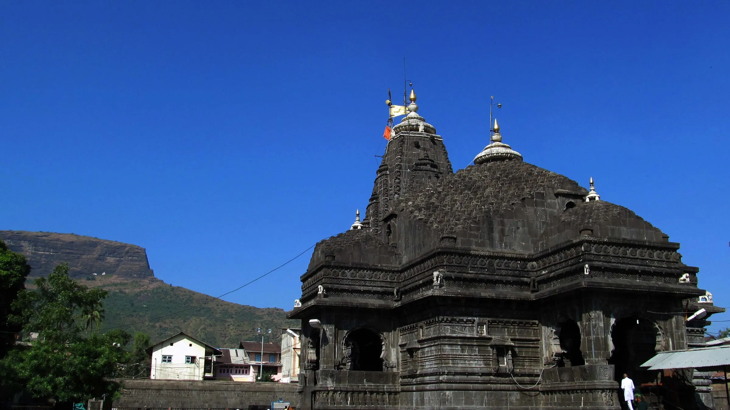 Trimbakeshwar Temple's stone spires under a blue sky, with the Brahmagiri hills behind