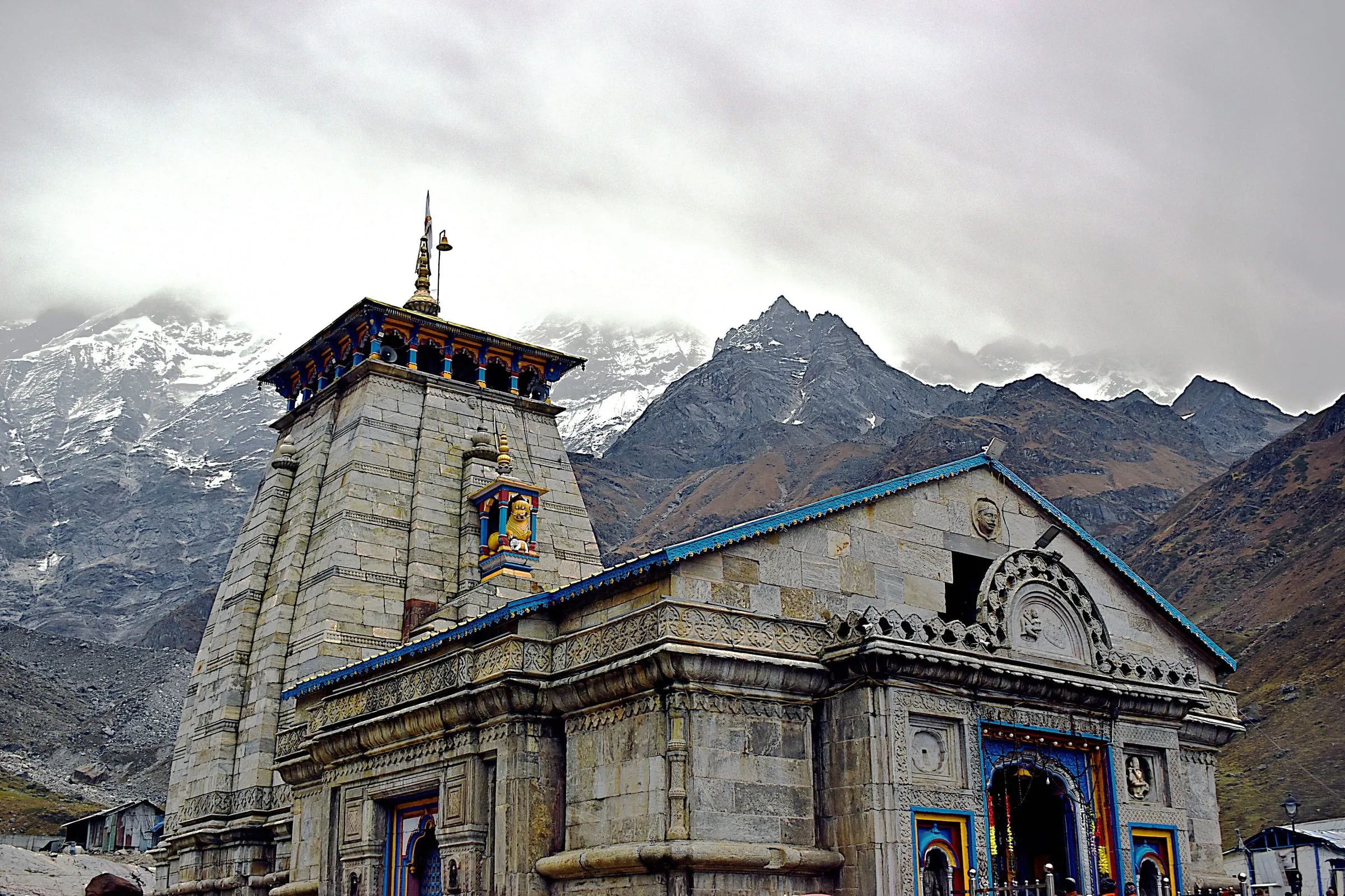 Kedarnath Temple's carved stone front under a cloudy sky, with mountains behind