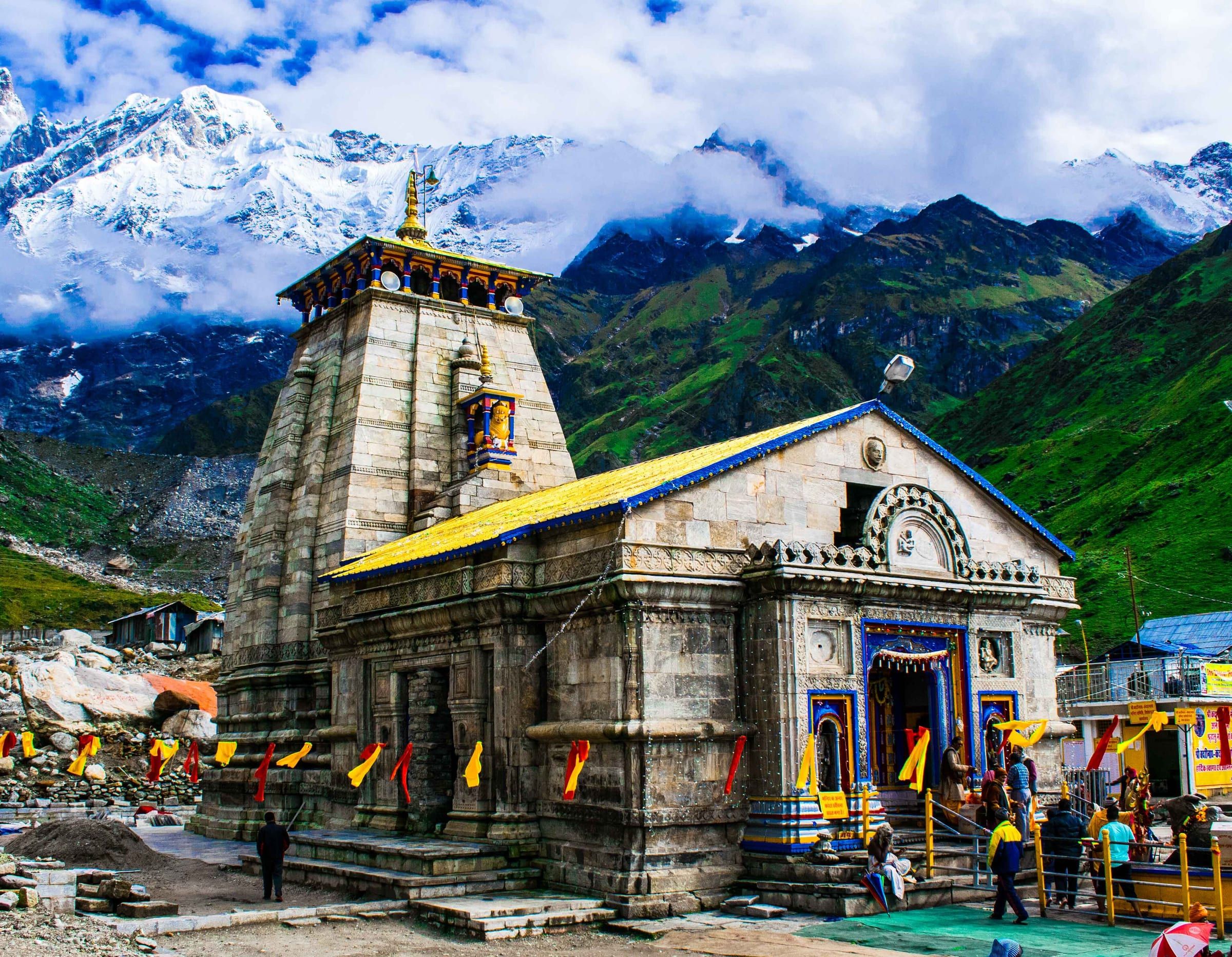 Kedarnath Temple's grey stone front and spire, with green slopes and snow peaks behind