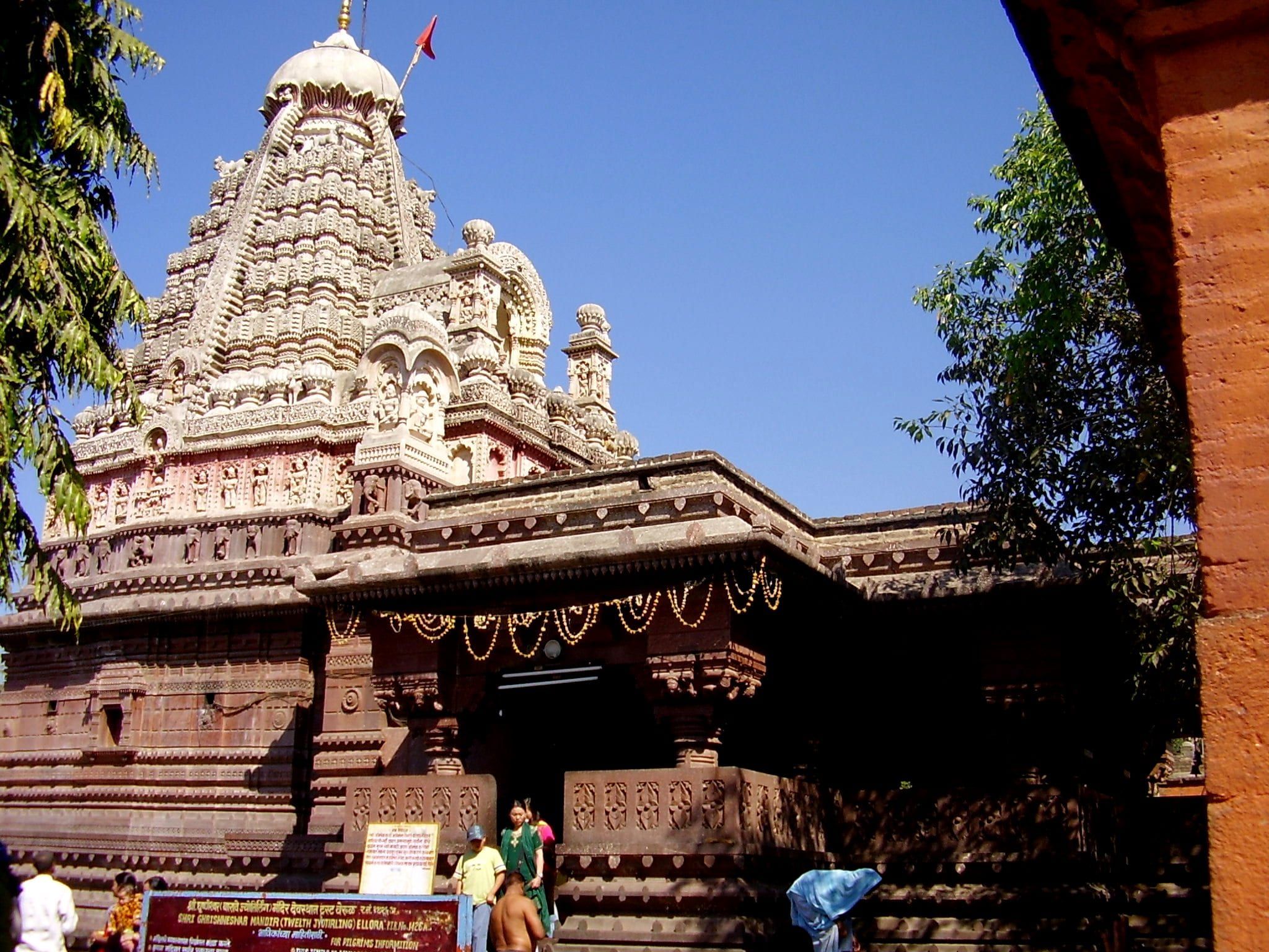 Grishneshwar Temple's red stone spire, covered in carvings, against a blue sky